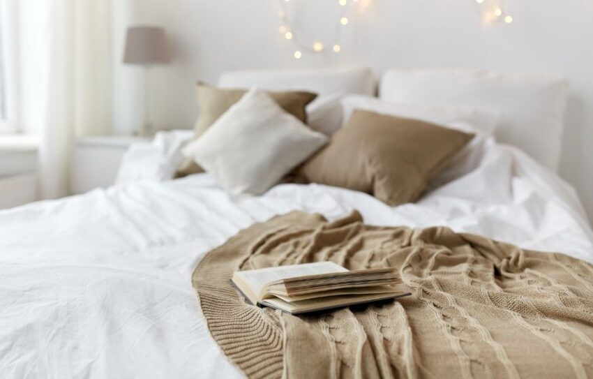 Bed with white bedding and grey and brown cushions. There is a brown throw with an open book.