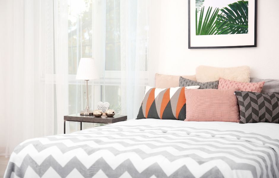 A Bed with zigzag patterned bedspread and a selection of cushions