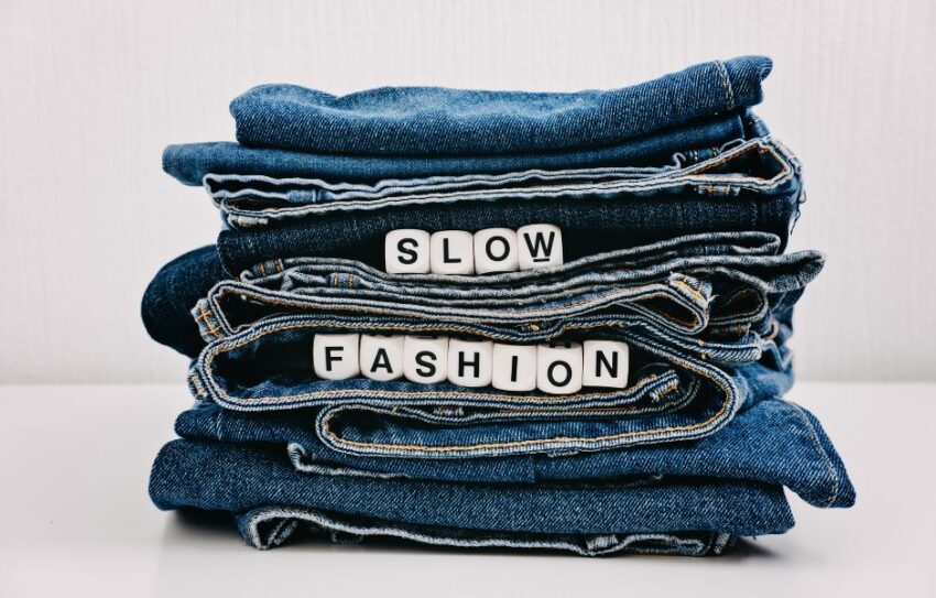 Several pair of jeans are folded and piled together. In between the folds are blocks which which spell out 'Slow Fashion'