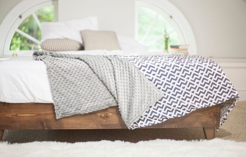 A brown wooden bed with a blue patterned blanket spread across it