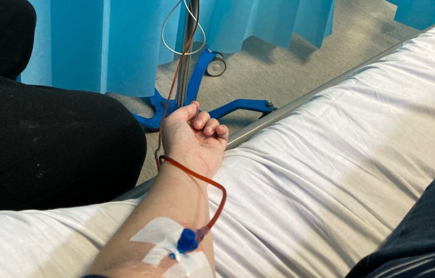 A hospital bed with a woman's armed hooked up to an iron drip