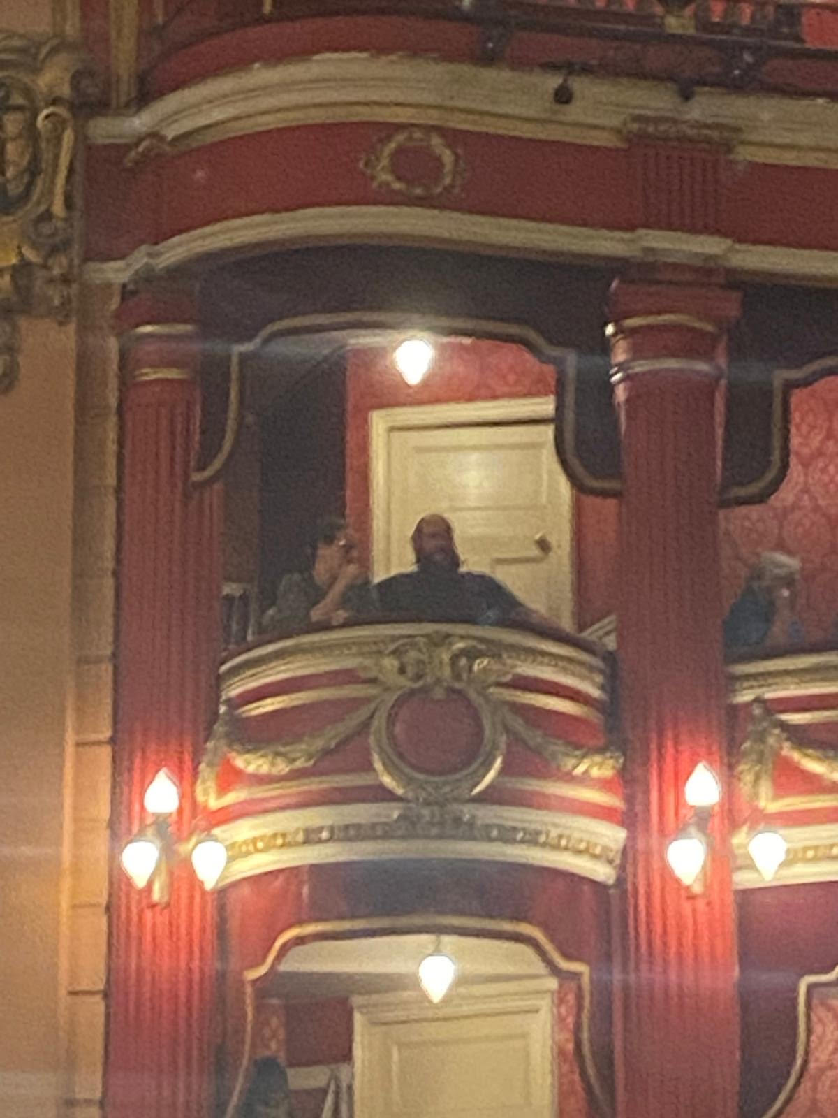 An image of myself and my husband sitting in a box at the Bristol Hippodrome. The box is red with gold decoration and there is a white door behind us