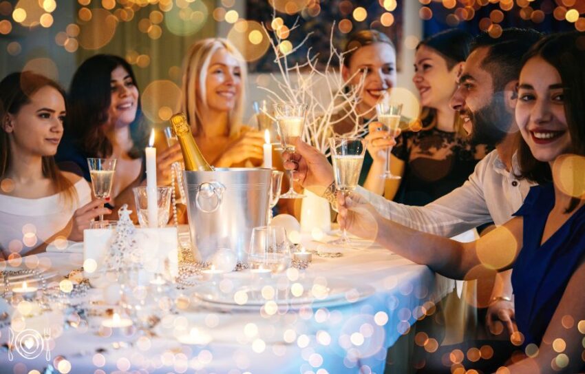 A group of girl friends hold up their glasses in a cheers pose over a table covered with plates and glassware