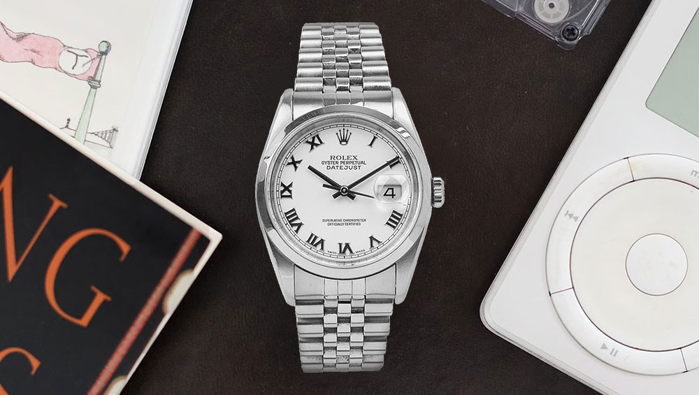 A silver Rolex Watch with a white face and black details. There is an ipod and a book in either side of it.