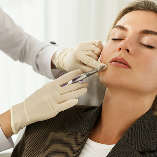 A woman is laying back slightly. She is getting an injection into her chin.