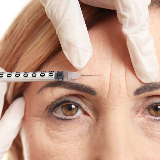 A close up of a woman's face. She is getting an injection into her forehead.