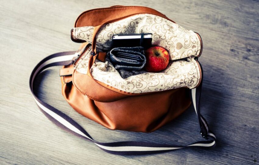 A brown leather handbag which is open - there is a purse, notebook and apple sticking out of the bag
