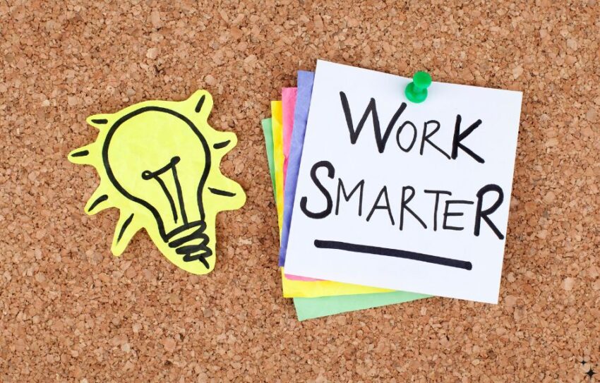 A corkboard has a yellow lightbulb sticker a post it note that says Work Smarter